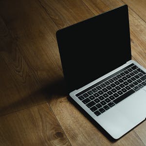 MacBook placed diagonally on a warm wooden floor with soft lighting.